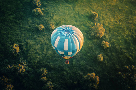 A hot air balloon drifts gracefully above lush green fields at dawn, showing the serene beauty of nature. The landscape reveals a patchwork of crops and trees.の素材