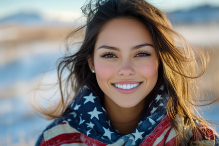 A young woman with long hair smiles warmly while wrapped in a scarf featuring star patterns. Snow-covered mountains are visible in the background under a clear blue sky.の素材