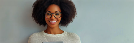 A woman with curly hair and glasses smiles warmly while standing in a bright office. Natural light illuminates the room, creating a welcoming atmosphere.の素材