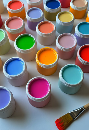 Brightly colored paint containers are organized on a workspace, showing a variety of hues suitable for artistic projects. A paintbrush with vibrant bristles is included.の素材