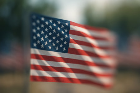 A vibrant American flag flutters gracefully in the wind at a memorial location. The sun casts a warm glow, highlighting the colors of the flag against a blurred backdrop.の素材