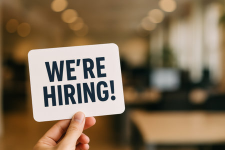 A person holds a hiring sign in a stylish office space with blurred backgrounds. The atmosphere suggests an inviting workplace looking for new talent.の素材