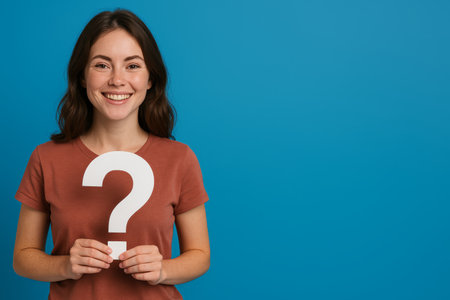 A woman with long hair smiles while holding a large question mark in front of a bright blue background. Her expression suggests curiosity and a desire for answers in a vibrant setting.の素材