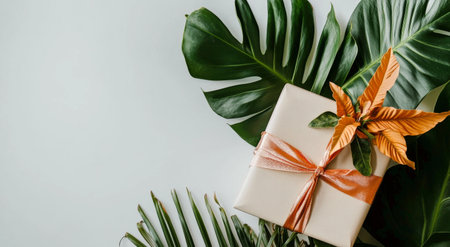 A beautifully wrapped gift box features a striking orange flower and green leaves on top. The soft ribbon adds a touch of elegance, perfect for any special occasion.の素材