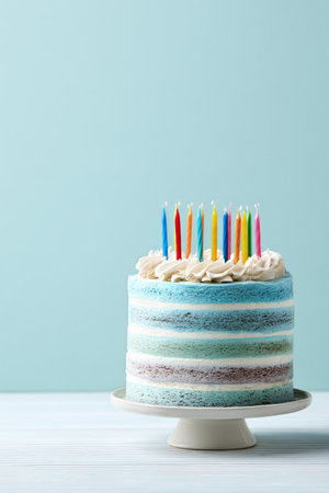 A vibrant blue birthday cake topped with multicolored candles stands on a white pedestal. The scene is festive and cheerful, perfect for a birthday celebration.の素材