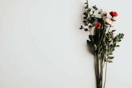Delicate flowers in shades of red and cream are artistically arranged with greenery against a light background, creating a peaceful and inviting atmosphere.の素材