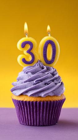 A colorful cupcake with fluffy purple frosting sits against a bright yellow background. Two candles shaped as the number 30 are lit, symbolizing a milestone birthday celebration.の素材