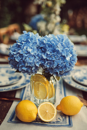 Bright blue flowers are arranged with fresh lemons in a clear glass vase, set on a table with a burlap runner, perfect for a cheerful indoor gathering.の素材