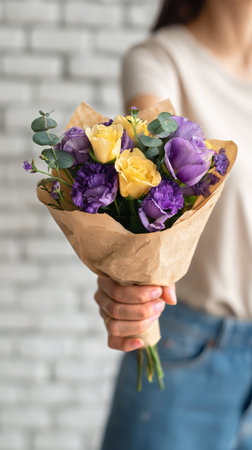 A person presents a vibrant bouquet featuring purple and yellow flowers.の素材