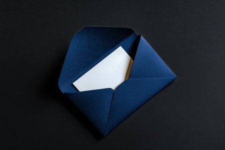A navy envelope is partially opened, revealing a blank white card inside, resting on a black surface, creating a clean and modern aesthetic.の素材