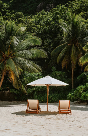 Two lounge chairs sit on a sandy beach beneath a large umbrella. Lush tropical plants and palm trees provide a vibrant backdrop under a sunny sky.の素材