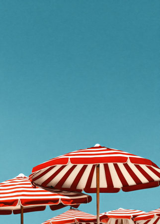 Brightly colored striped umbrellas stand in a row, offering shade to beachgoers enjoying the warm weather under a clear blue sky with scattered clouds.の素材