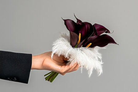 A hand showcases a stunning bouquet featuring deep purple calla lilies surrounded by soft white feathers, set against a neutral backdrop, enhancing the bouquets elegance.の素材