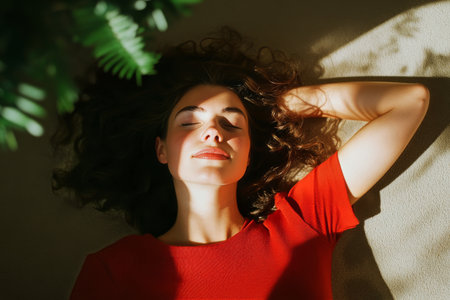 A woman with curly hair rests calmly on a soft surface, basking in sunlight. Her relaxed posture and peaceful expression create a warm, tranquil atmosphere in the room.の素材