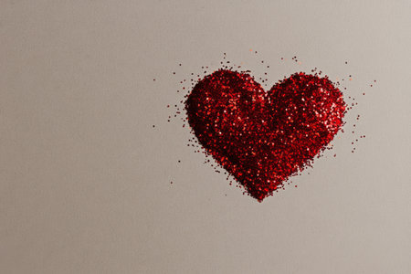Red glitter is arranged in the shape of a heart on a light plain background, perfect for craft projects, decorations, or special events.の素材