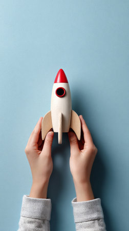 Two hands grasp a colorful wooden rocket, showcasing creativity and imagination against a soft blue backdrop. A playful expression captures the joy of childhood exploration.の素材