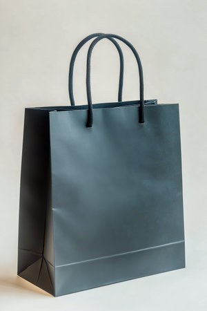 A black shopping bag with sturdy handles is positioned against a soft light background. Ideal for showcasing retail products or promotional offers in an elegant manner.の素材