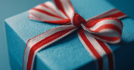 A beautifully wrapped gift box in blue with a bright red and white ribbon sits against a dark backdrop, suggesting a festive occasion. Perfect for any celebration or special event.の素材