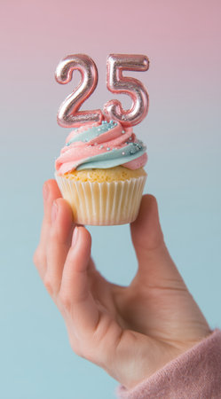 A hand presents a colorful cupcake decorated with pink and blue frosting and sparkling toppings, featuring a shiny number 25 candle on top, perfect for a milestone birthday.の素材