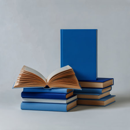 Blue hardcover books are stacked together, with one book opening and displaying its pages. The soft light highlights the textures and colors of the books on a plain backdrop.の素材