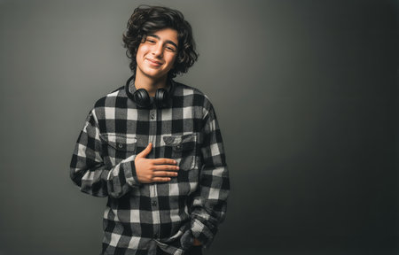 A young man stands confidently with a smile, wearing a black and white plaid shirt and headphones. The background is simple, focusing on his relaxed expression and casual style.の素材