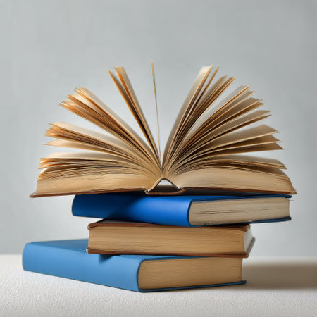 Blue hardcover books are stacked together, with one book opening and displaying its pages. The soft light highlights the textures and colors of the books on a plain backdrop..の素材
