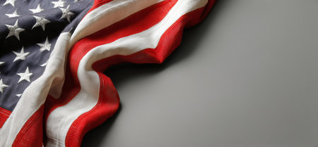 A folded American flag rests on a gray surface, showing its red, white, and blue colors. The stars and stripes represent freedom and national pride in this simple yet powerful scene..の素材