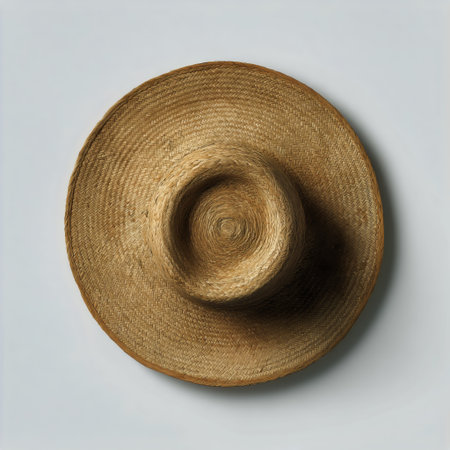A straw hat with a wide brim is centered on a light surface. The hat features intricate weaving, showing its natural texture and design. It has a simple yet stylish look.の素材