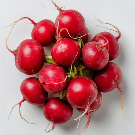 A cluster of vibrant red radishes with their green tops visible is displayed on a light background, showing their freshness and perfect for adding crunch to meals.の素材