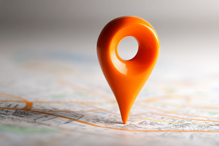 A bright orange location pin sits on a detailed map, pointing to a specific area. The pin appears glossy and reflects light, drawing attention to its position on the map..の素材