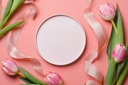 A simple scene features a round plate placed on a soft pink background surrounded by vibrant tulips and decorative ribbon, creating a fresh spring aesthetic.の素材