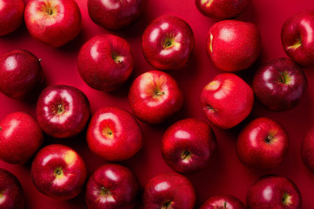 A collection of vibrant red apples is neatly spread across a striking red surface. Their shiny skin reflects light, enhancing their fresh, appetizing appearance..の素材
