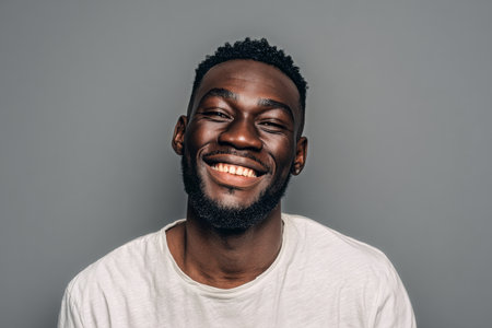 A man with a broad smile and short hair poses against a simple gray backdrop. His joyful expression suggests a lighthearted mood and a sense of confidence.の素材