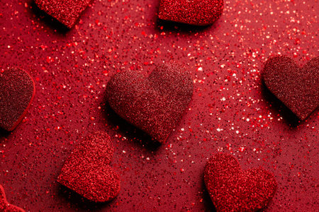 Scattered red heart shapes with sparkly surfaces lay on a dark backdrop, creating a festive look perfect for Valentines Day celebrations or romantic occasions..の素材