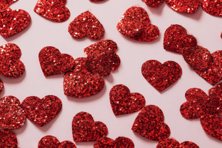 A variety of red glittery heart shapes is scattered across a soft light-colored background, ideal for festive events and expressing love. Perfect for celebrations or crafts.の素材