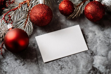A blank card rests on a smooth marble surface, framed by festive red and silver ornaments along with green pine branches, creating a cozy holiday atmosphere..の素材