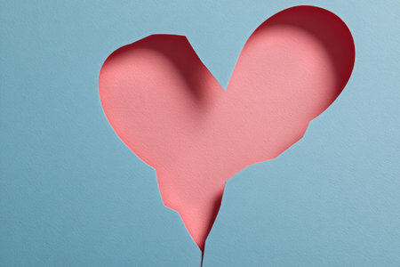 Two pink paper hearts sit against a light blue backdrop, showcasing a broken heart design that symbolizes feelings of loss and heartbreak. The simple colors enhance the emotional theme..の素材