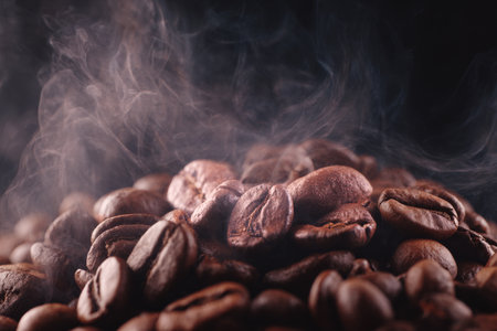 Coffee beans scatter across a surface, releasing steam as they cool. The rich brown color and visible texture create an inviting atmosphere for coffee lovers..の素材