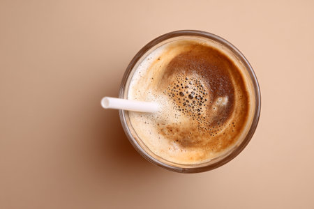 A creamy coffee drink sits in a glass, topped with frothy bubbles. A straw is placed inside, inviting a refreshing sip during a relaxing afternoon.の素材