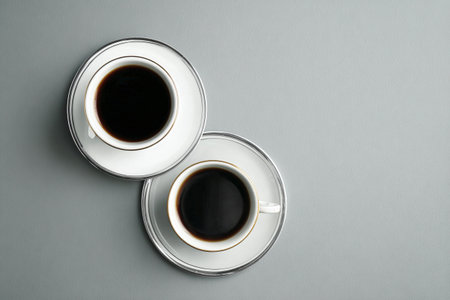 Two stylish coffee cups, one silver and one white, rest on matching saucers. The rich coffee inside invites warmth and comfort, perfect for a peaceful morning moment..の素材