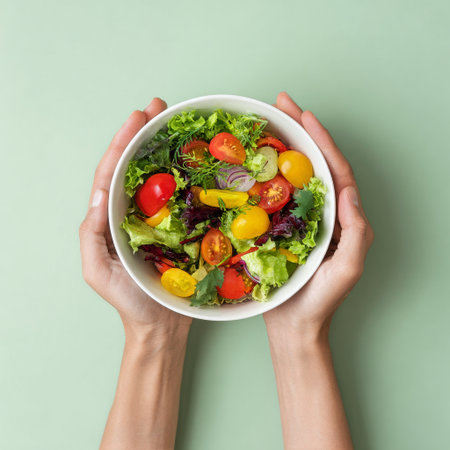 A pair of hands hold a bowl filled with a vibrant salad containing various greens and cherry tomatoes. The scene is clean with a soft, light background.の素材