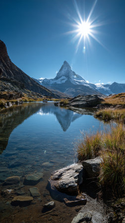 Clear blue sky shines over the Matterhorn as its peak reflects in the still waters of a mountain lake. Lush grass frames the lake, creating a serene natural landscape.の素材