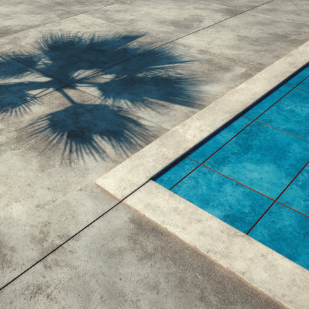 Light blue water of a pool reflects under the sun, with shadows of palm leaves creating an artistic design on the concrete surface nearby.の素材