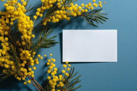 Bright yellow flowers are arranged beside a blank card against a blue background, creating a vibrant and cheerful scene suitable for design projects or personal notes.の素材