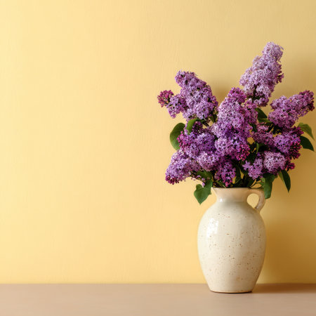 A charming vase holds vibrant purple lilac flowers, set against a warm yellow wall. The arrangement brings a fresh and inviting touch to the cozy indoor space.の素材