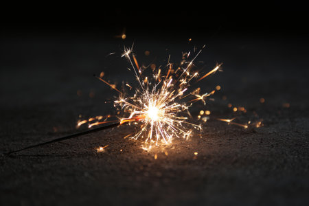 A sparkler burns brightly on a dark surface, sending sparks flying in all directions, creating a festive atmosphere. Perfect for celebrations and nighttime festivities.の素材