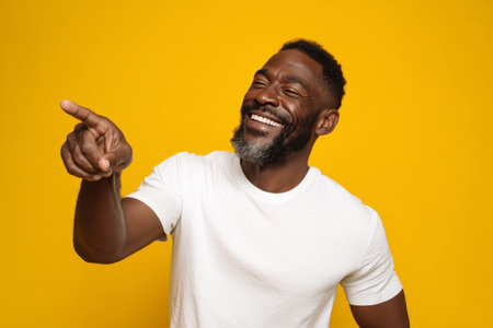 A man with a beard is laughing and pointing cheerfully against a vivid yellow background. His expression shows joy, creating a lively atmosphere full of happiness.の素材