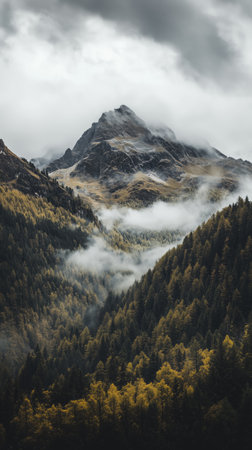A stunning mountain rises above a lush valley filled with trees in autumn hues. Clouds weave through the landscape, creating a tranquil and mystical scene.の素材