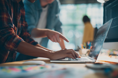 Group members actively discuss ideas and review details on a laptop screen during a meeting in a modern office. The atmosphere is collaborative and productive.. Details matter.の素材