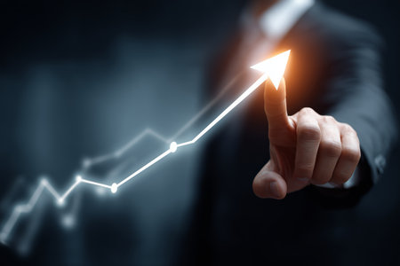 A confident business professional points at a glowing trend upward line on a digital graph in a dark office. The atmosphere suggests focus on growth and success in business.の素材